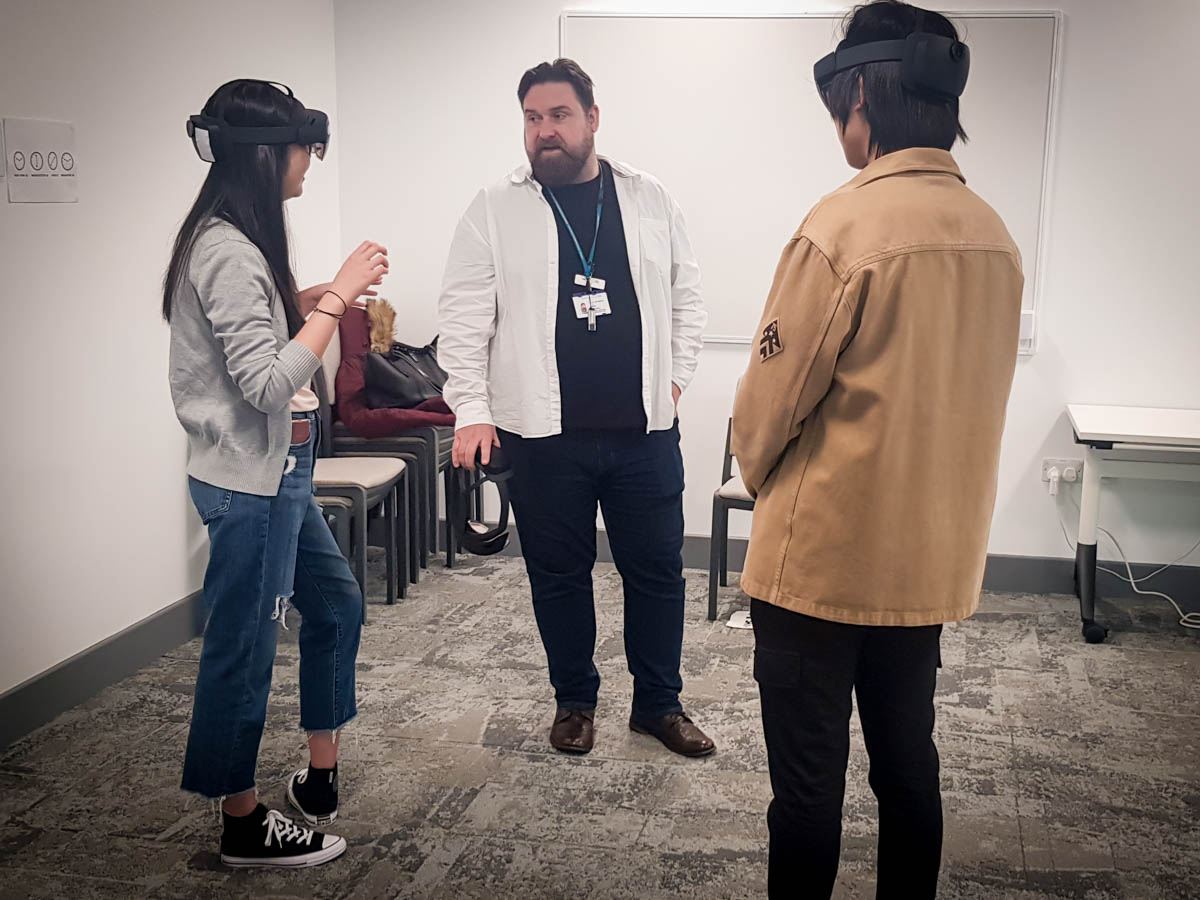Three people stood in a room. Two are wearing Microsoft HoloLens headsets.